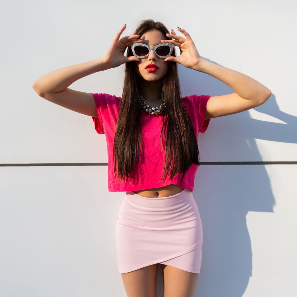Fashionable brunette woman in summer clothes  and sunglasses posing over white urban background.