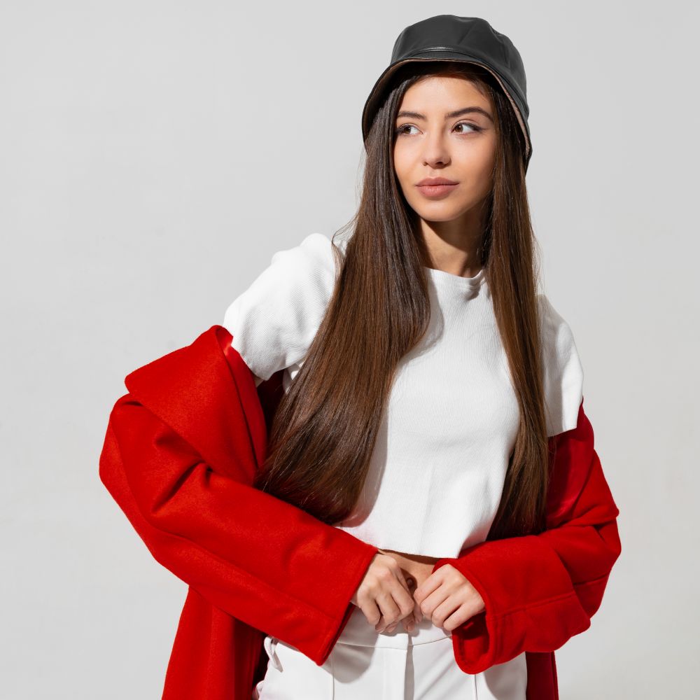 Trendy winter accsesorises. Pretty girl in black hat and red coat  raised hands and holding cap in studio on white background.