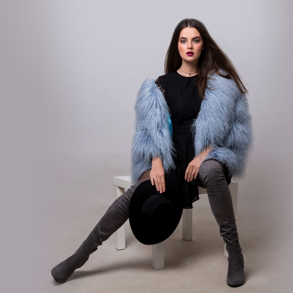 Sexy brunette woman in trendy  blue fur jacket and velvet thight high boots posing in studio on grey background.