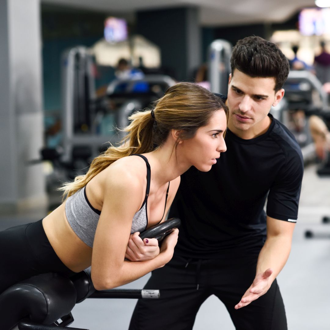 Personal trainer helping young woman lift weights while working out in a gym