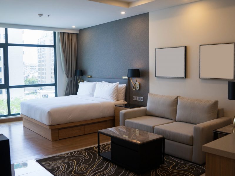 Cozy studio apartment design with bedroom and living space. Hotel room panoramic window, double bed, sofa and coffee table. Urban apartment concept