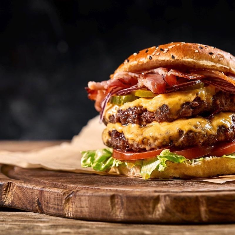 Juicy American burger, hamburger or cheeseburger with two beef patties, with sauce and basked on a black background. Concept of American fast food. Copy space.