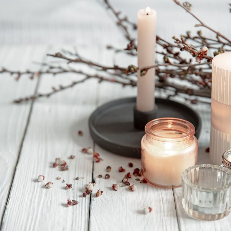 Cozy composition with flaming candles and young tree branches on a wooden surface in the Scandinavian style.